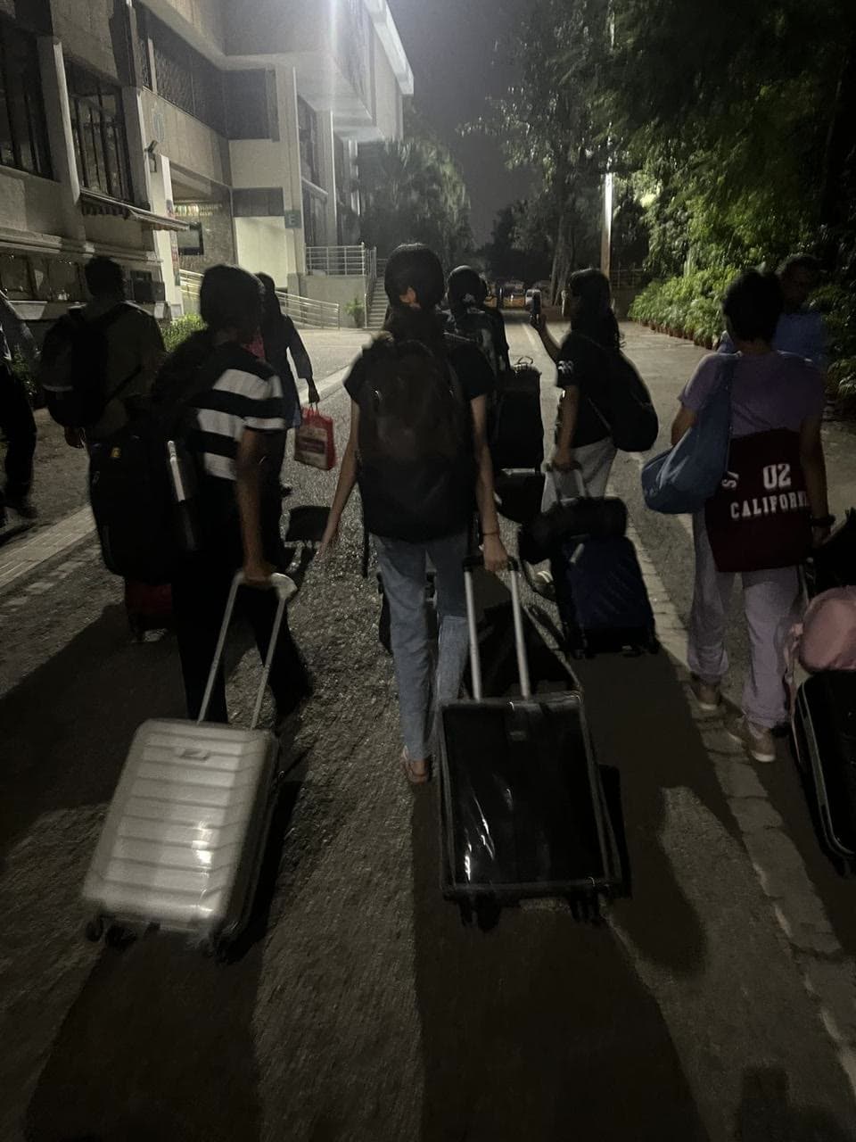 The group wheeling suitcases along a road after dark