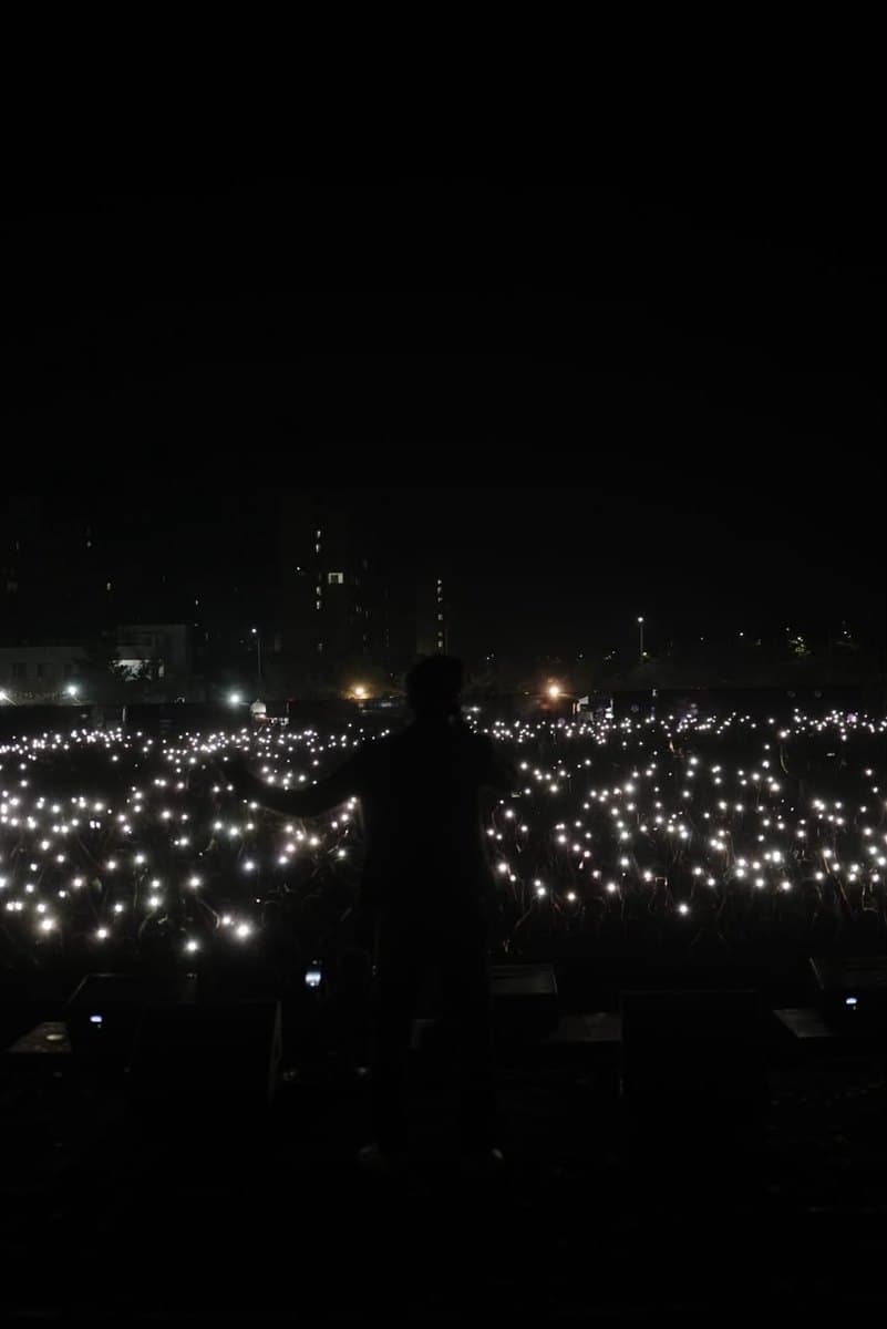 An artist on stage facing a field of raised phone lights in the dark