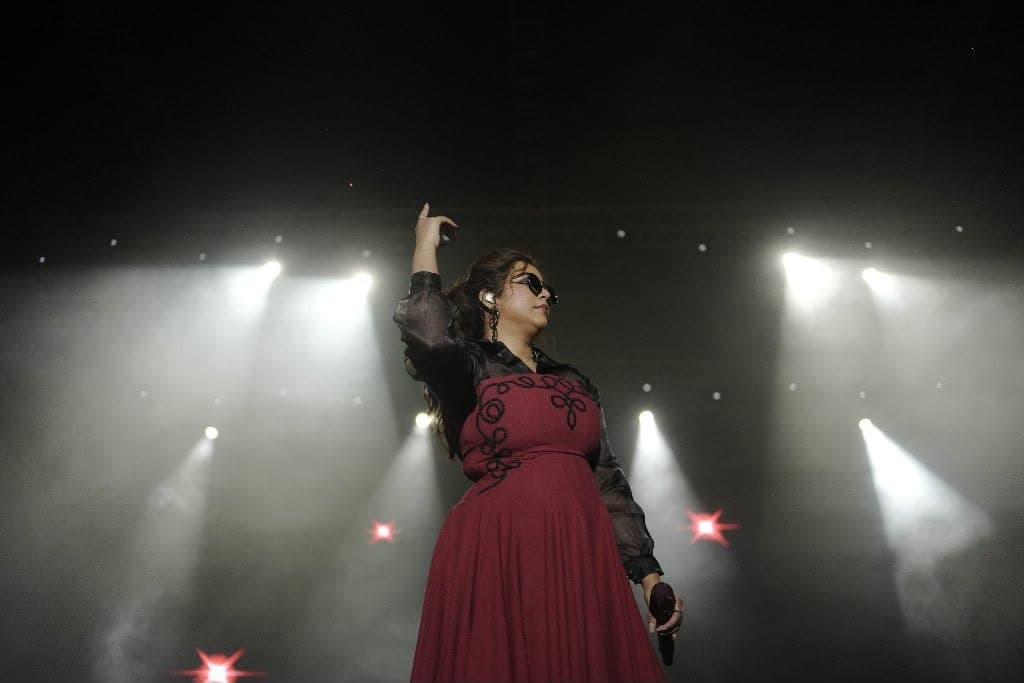 A singer in a red dress on the main stage, spotlights fanned out behind her