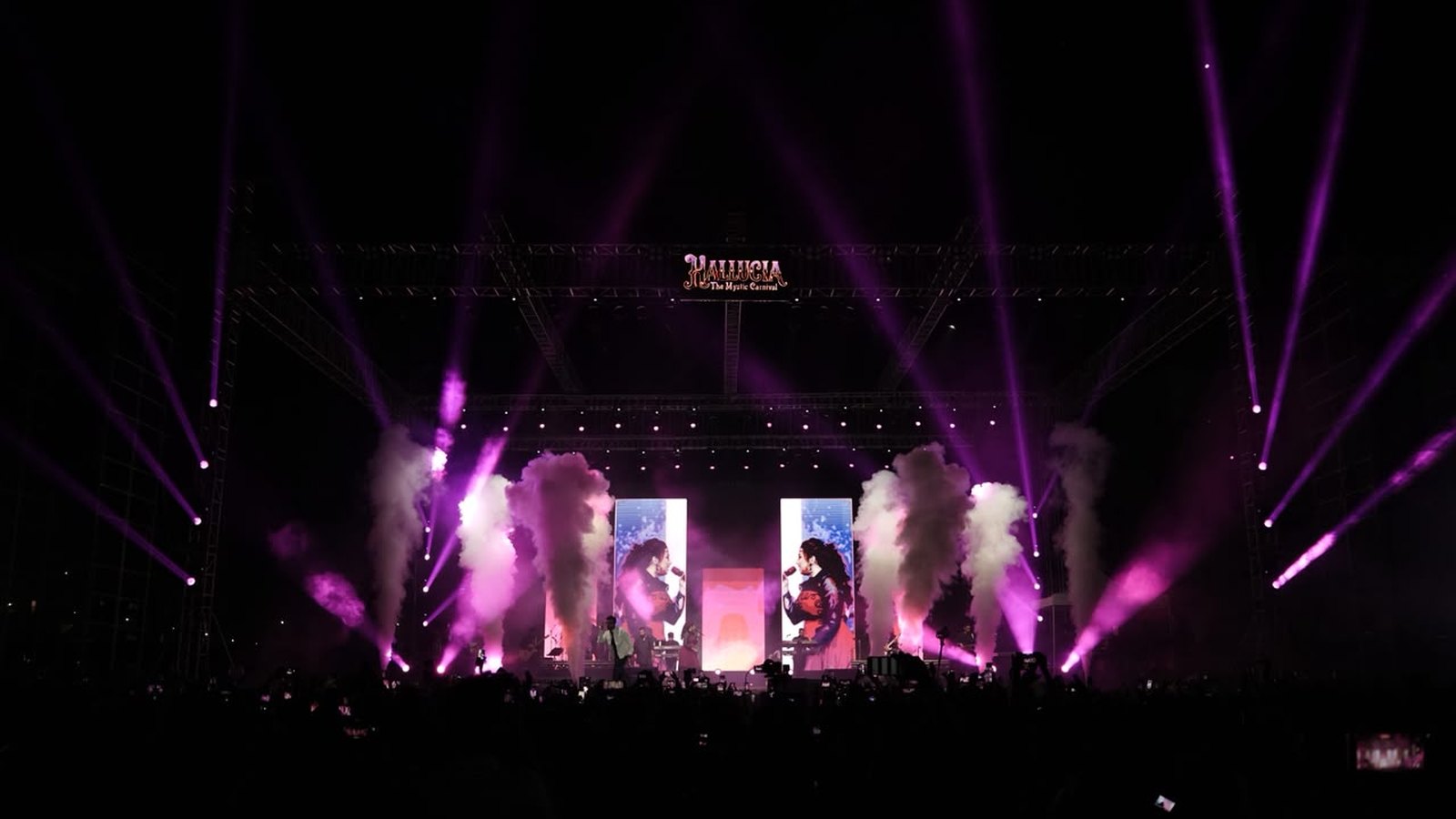 The HALLUCIA main stage at night under purple beams and smoke, the crowd silhouetted below
